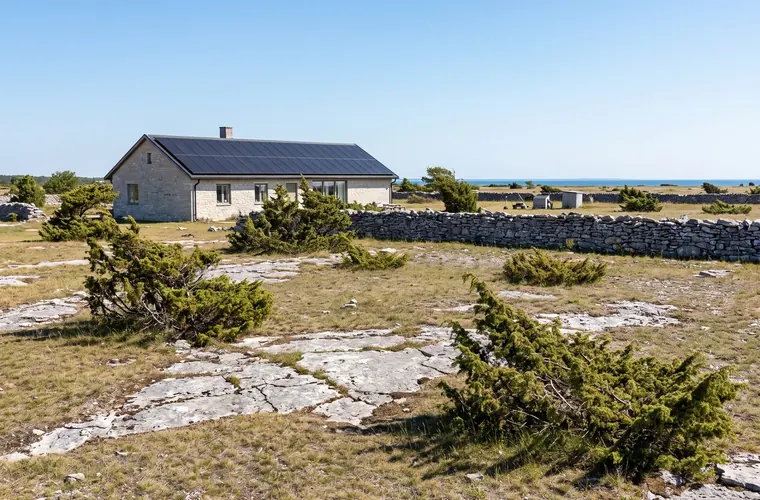 Kalkstenshus på Gotland med solceller på taket, alvarmark och havet i bakgrunden